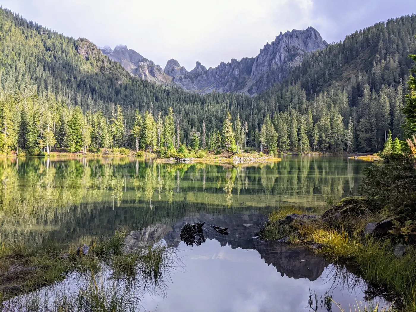 A aquamarine lake ringed by trees and rocks under a slightly overcast sky. The water is still and reflects the surrounding landscape.