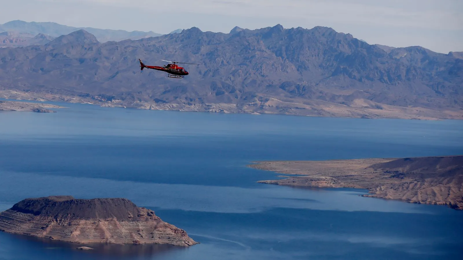 A bright red sightseeing helicopter soars above Lake Mead on a scenic flight towards the Grand Canyon from Las Vegas.