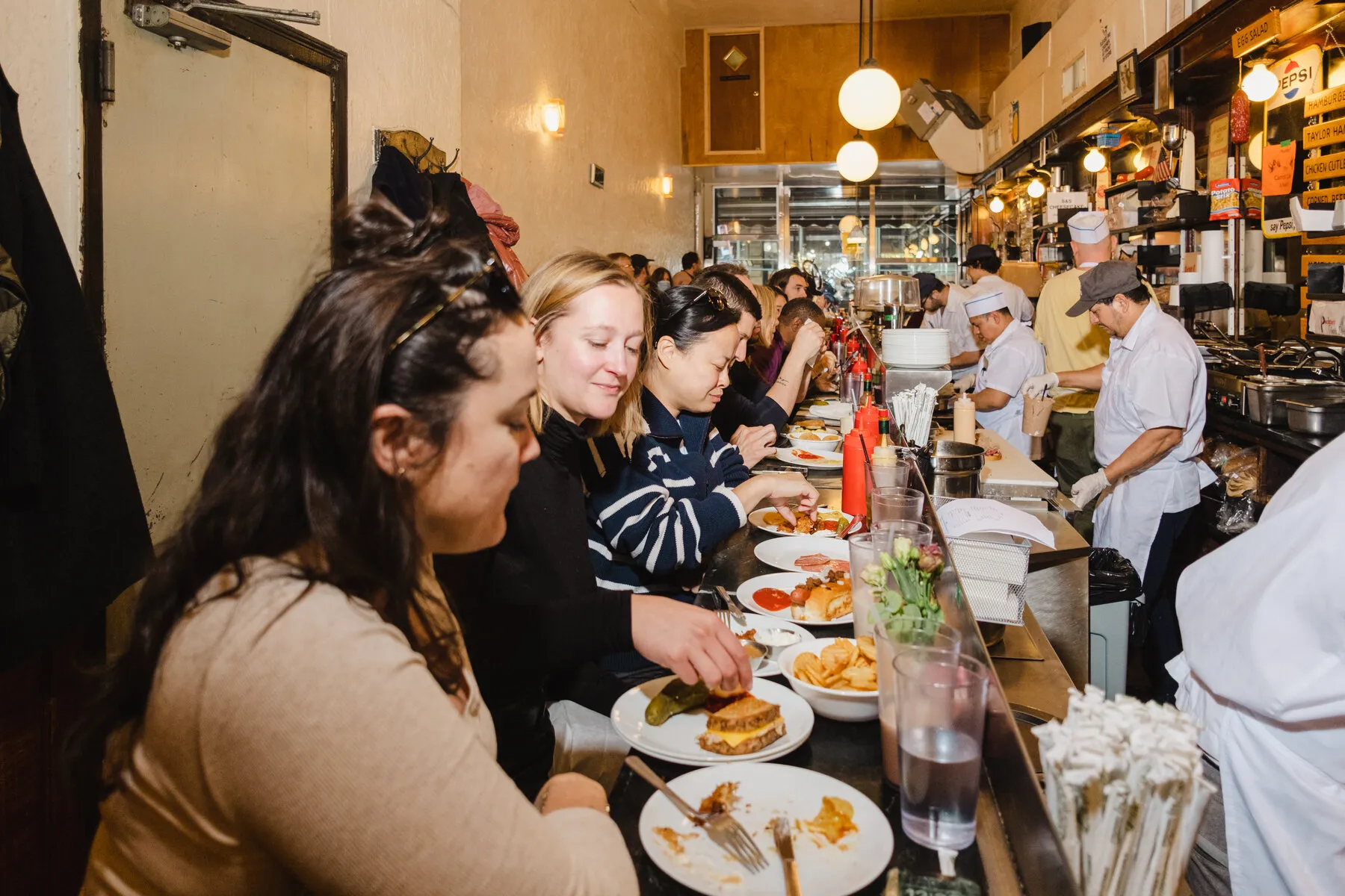A bustling lunch counter at S &amp; P Lunch, with customers seated and staff preparing food.