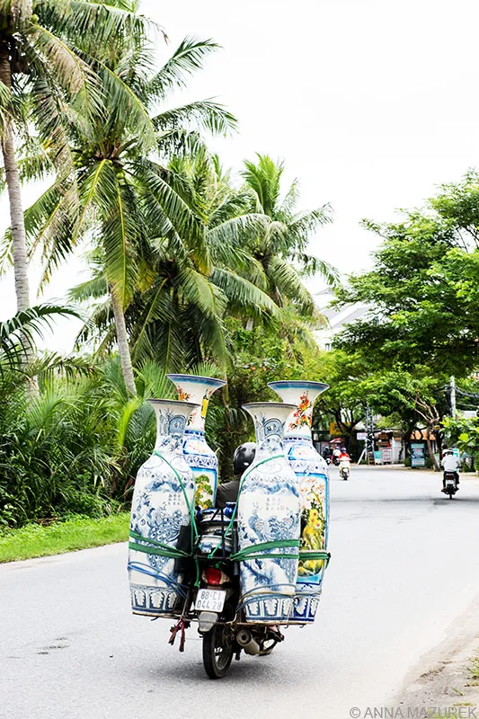 A bustling street scene in Hanoi, Vietnam, filled with motorbikes navigating through traffic, with buildings and shop signs lining the sides.