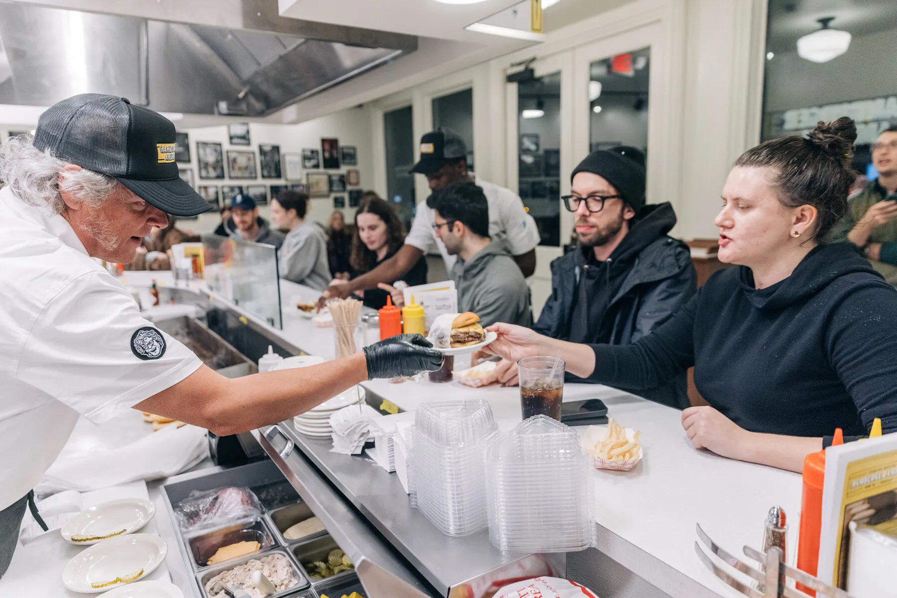 A busy counter scene at Hamburger America with staff making burgers and customers eating.