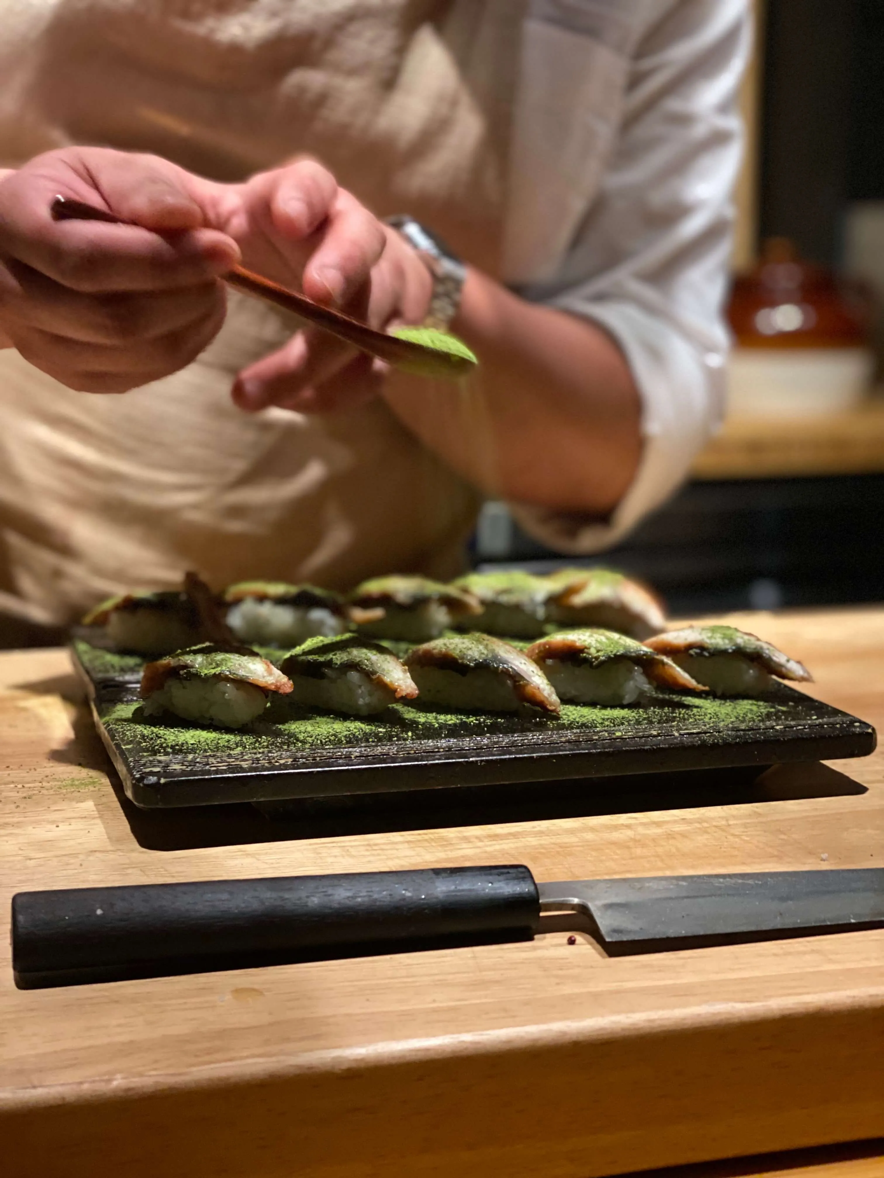 A chef presenting seared sushi pieces with creative toppings at Sushi By Scratch near Austin