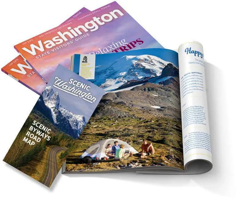 A collection of physical Washington State Visitors Guides and road maps stacked together