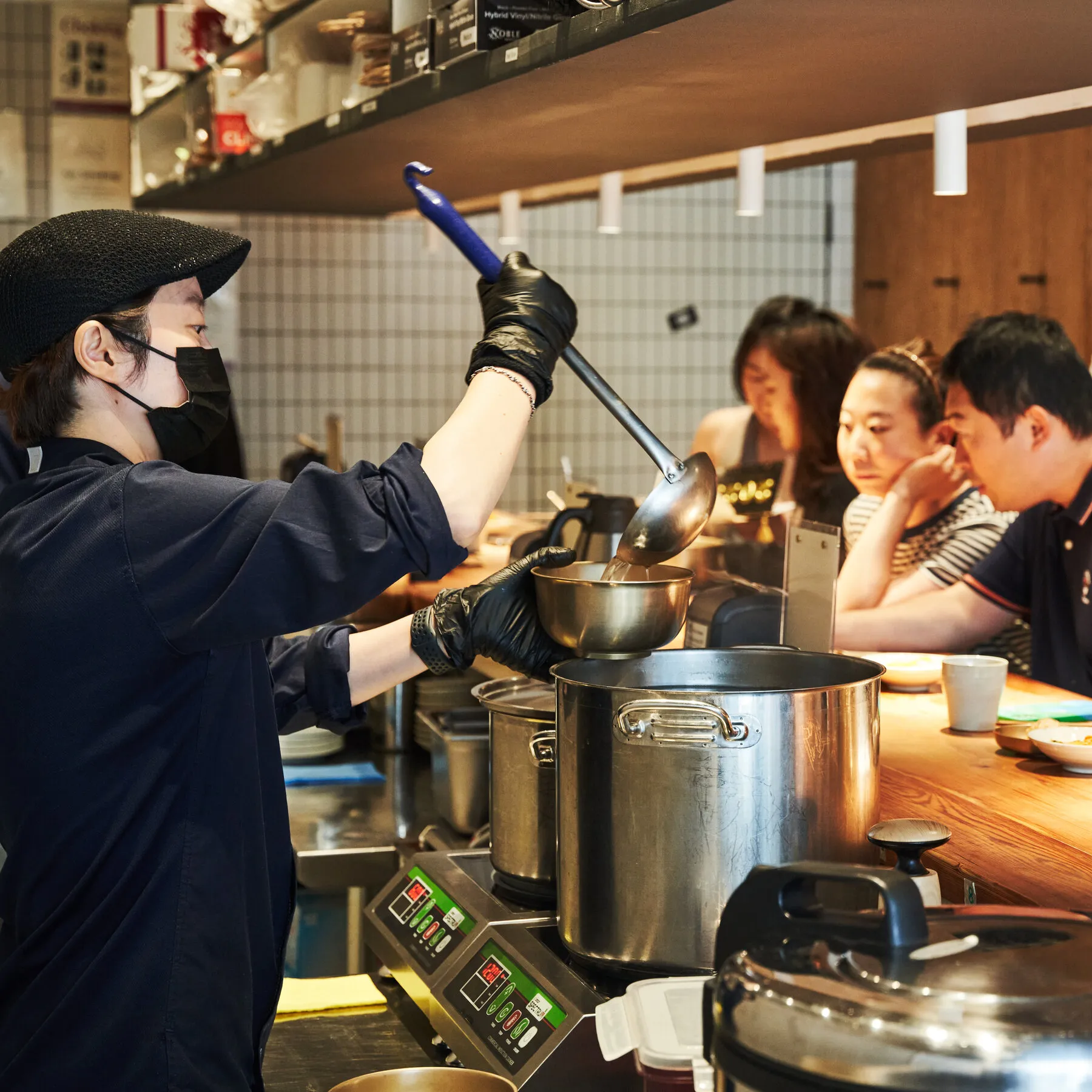 A cook at Okdongsik ladling clear pork broth into a bowl for a customer at the counter, showing the restaurant's focused setup.
