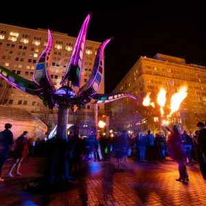 A crowd under a fire display and light sculpture at the Portland Winter Light Festival, one of the seasonal fun things to do in Portland