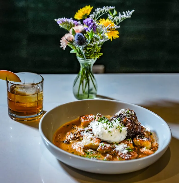 A farm-to-table dish, cocktail, and fresh flowers on a table at Till Neighborhood Bistro &amp; Bar in Colorado Springs.