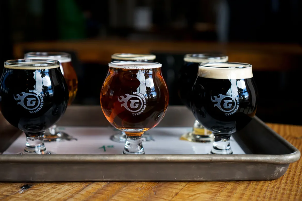 A flight of six small glasses of craft beer on a wooden paddle