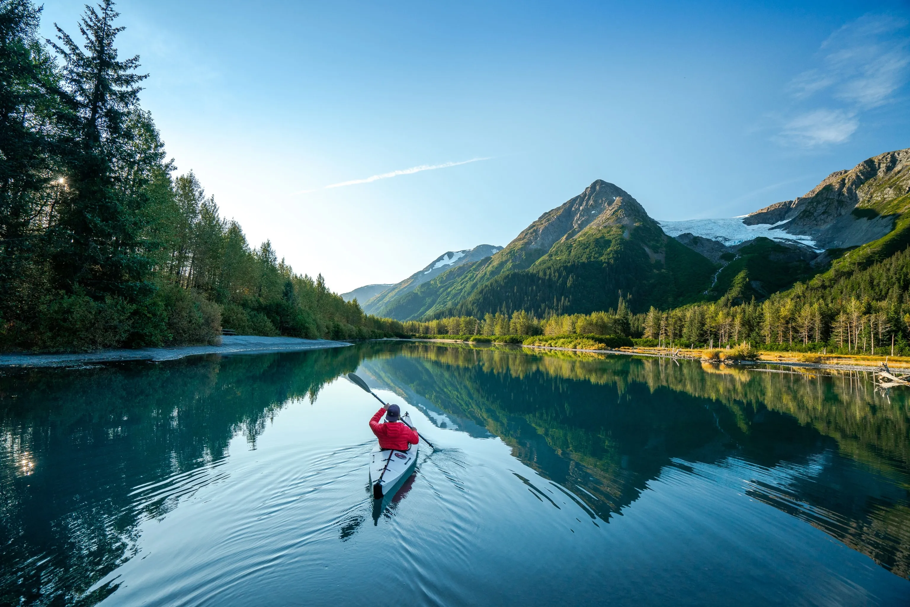 A kayaker paddles on a clear Alaskan river, showcasing outdoor adventures when visiting cities in Alaska.