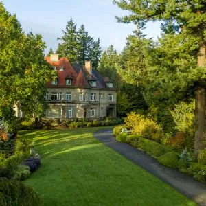 A large stone mansion with a red roof surrounded by trees, Pittock Mansion in Portland