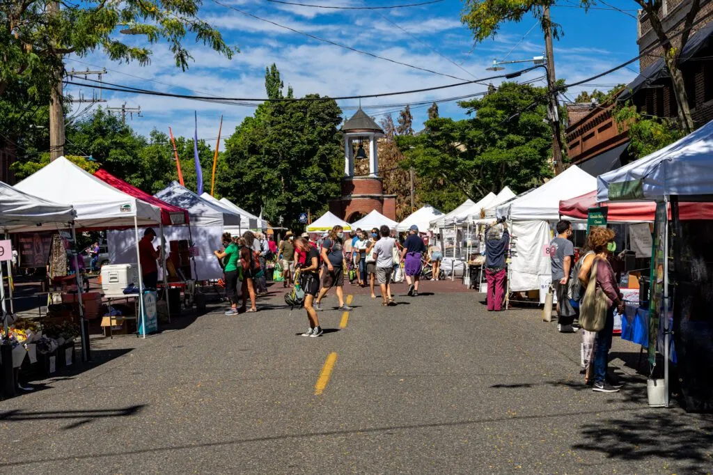 A lively outdoor scene with stalls and people, showcasing the vibrant atmosphere of the Ballard Farmers Market on a Seattle Weekend Trip