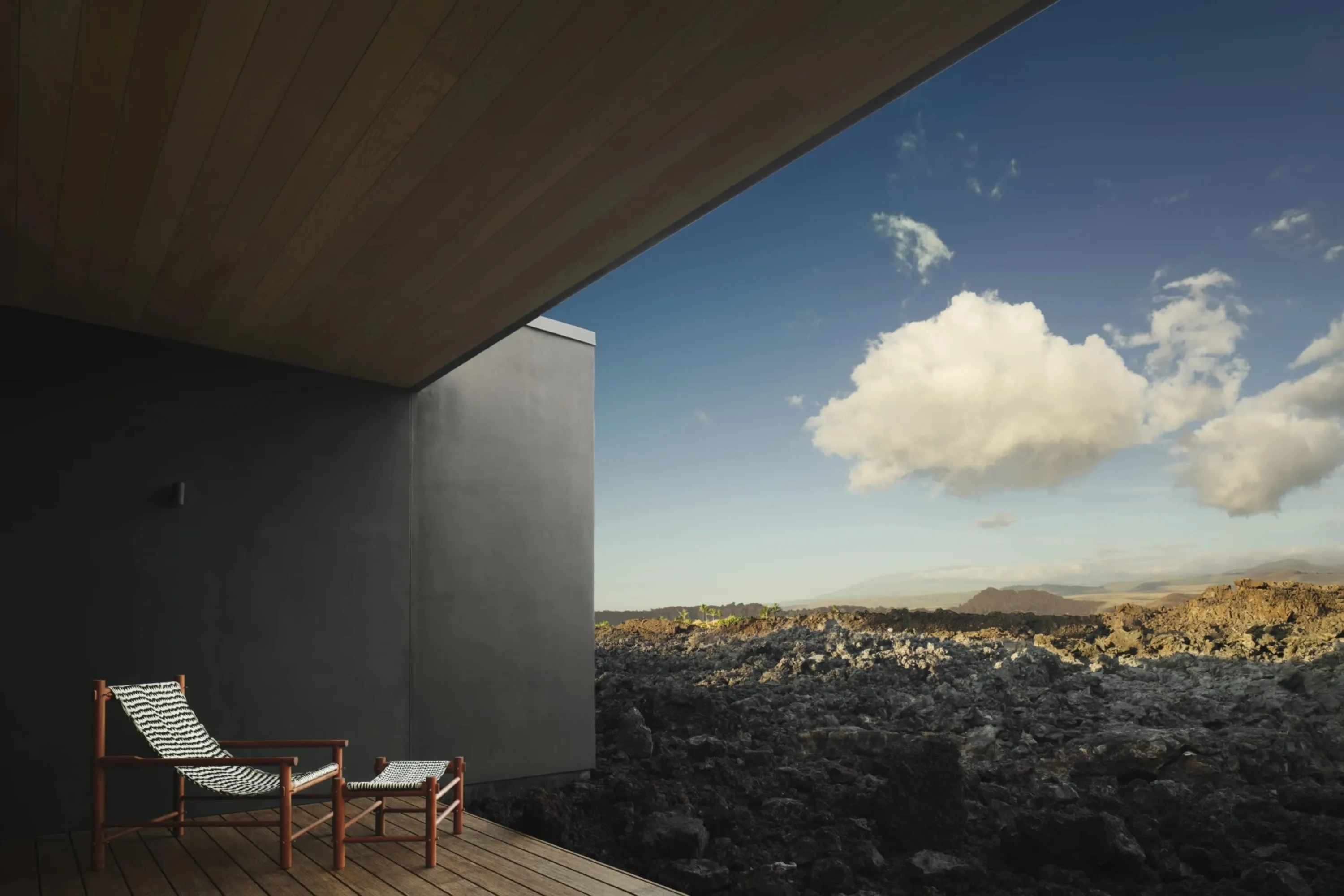 A lone lounger sits on a hardwood patio with a sleek awning, overlooking a bed of black lava rocks