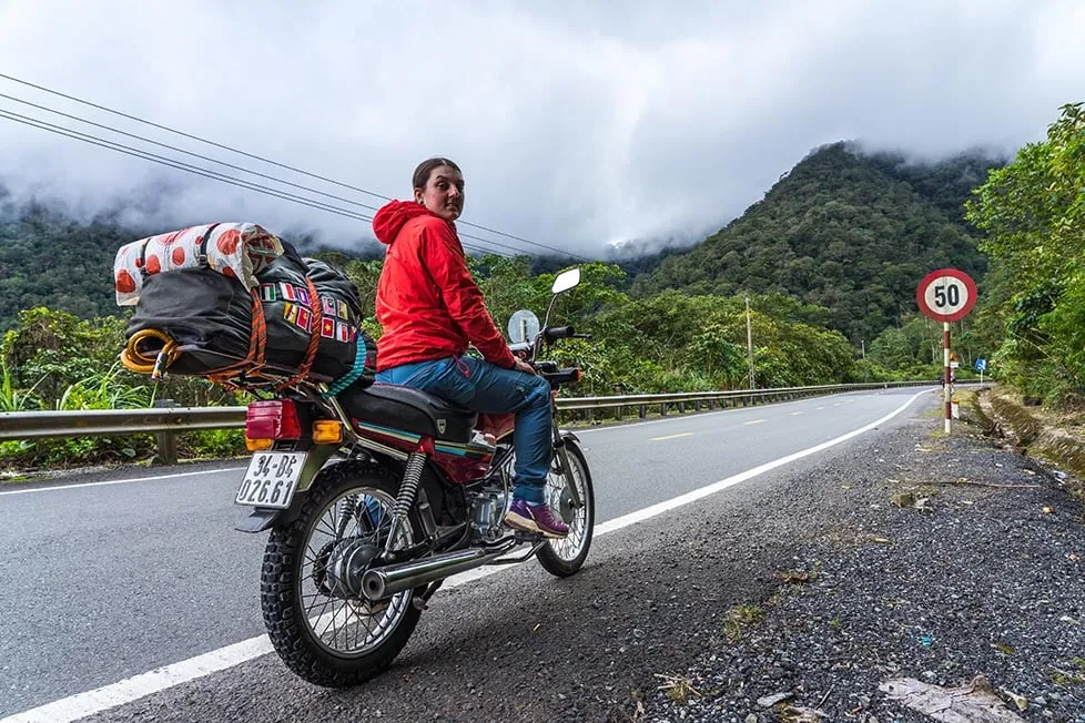 A motorbike parked on a mountain road overlooking misty valleys in the Vietnamese highlands, a highlight for adventurous backpackers.