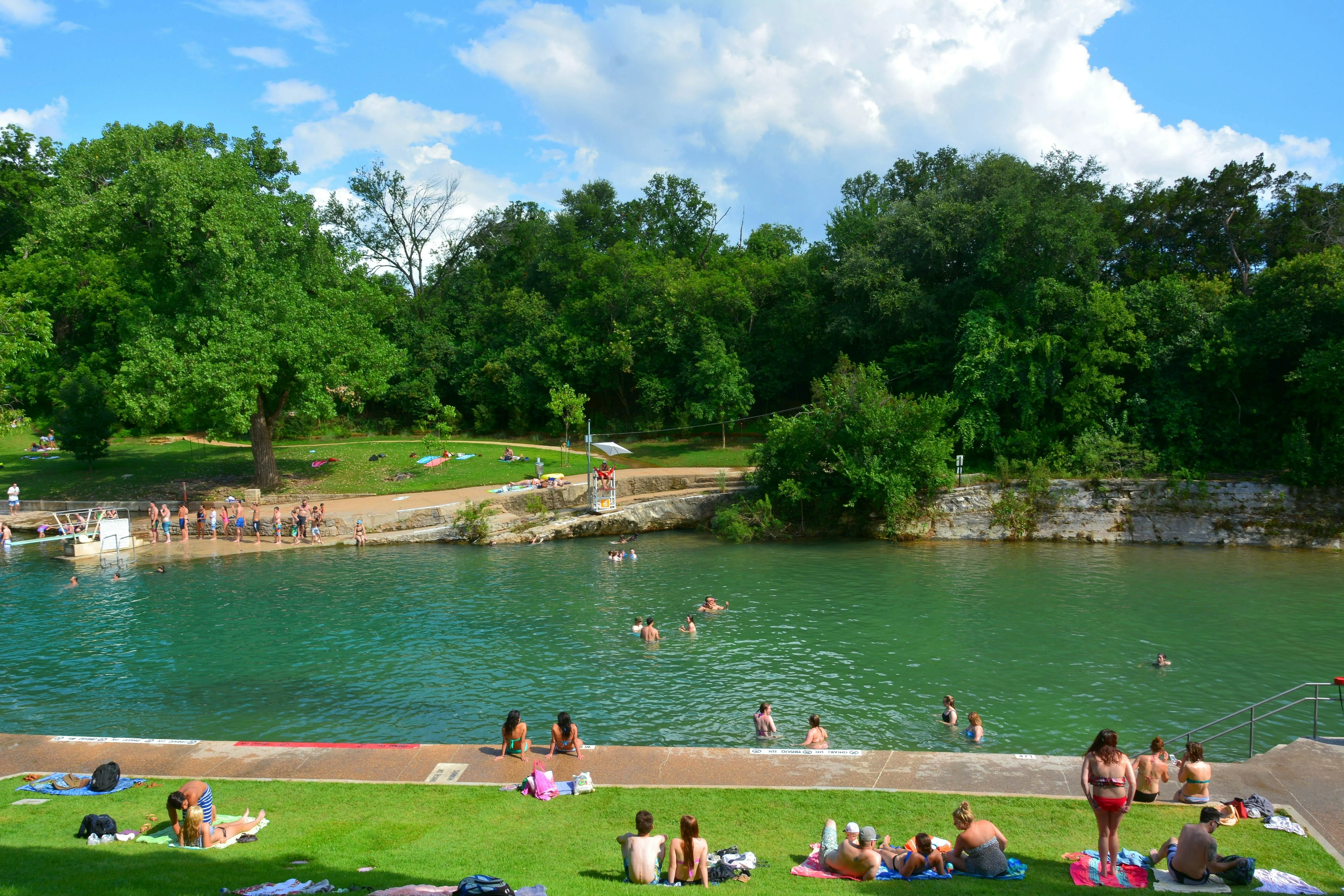 A natural pool with people swimming and green trees around