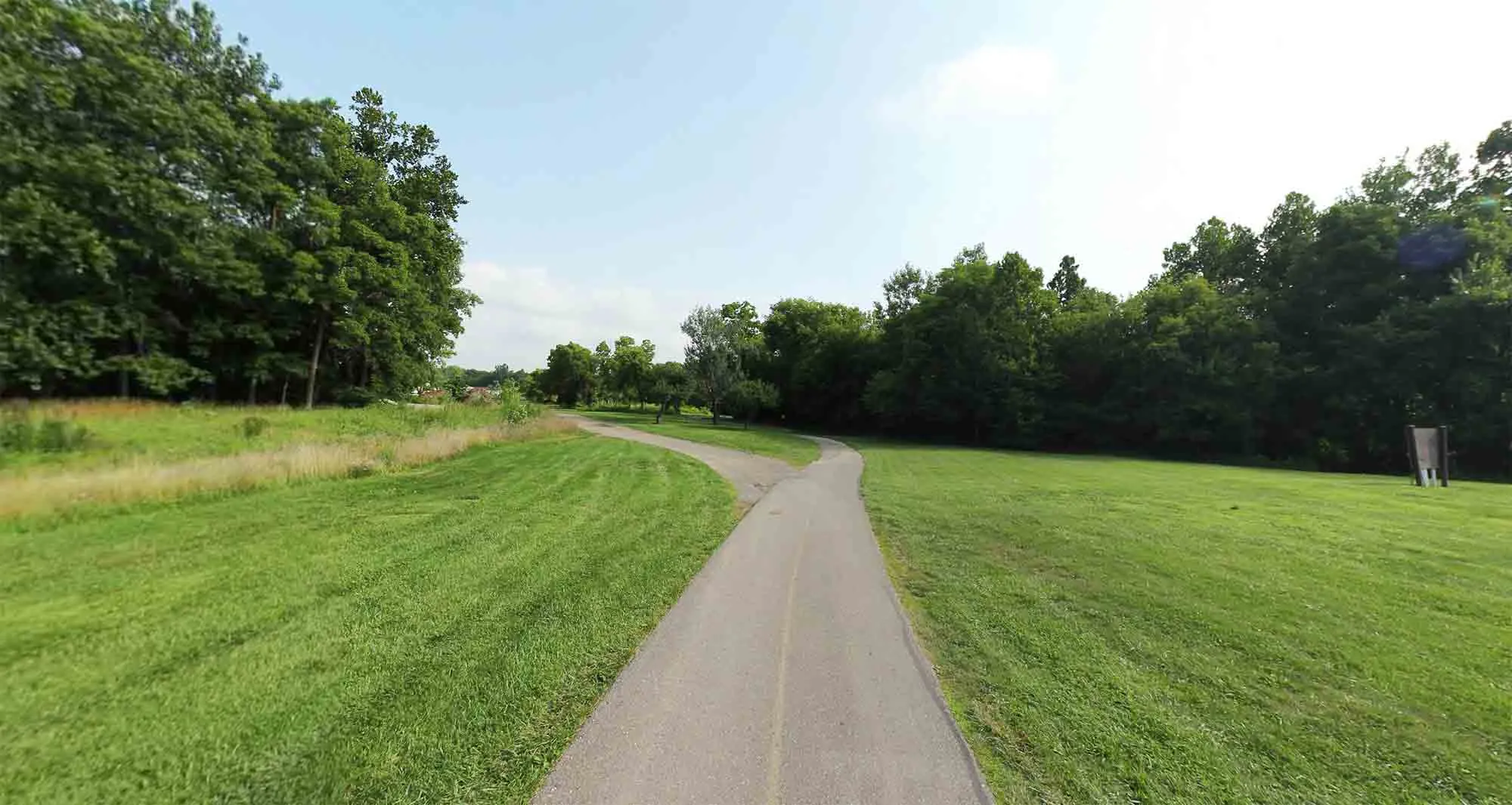 A paved trail surrounded by trees and greenery, part of the Downriver Linked Greenways system