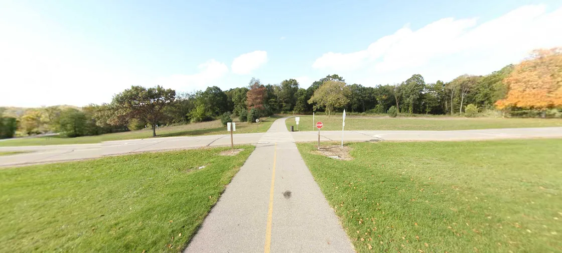 A paved trail winding through a park with mature trees, part of the Milford and Kensington Metropark Trail system