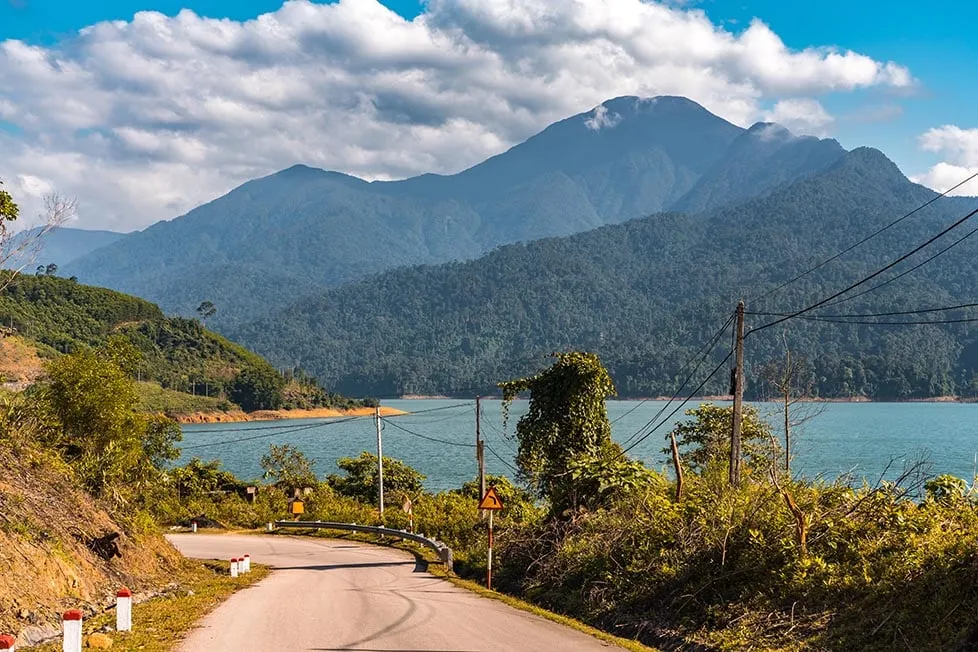 A person paddling a traditional wooden boat on a tranquil lake with mountains in the background in Vietnam.