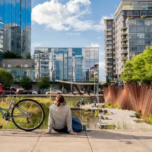 A person with a bicycle sitting near a pond in Tanner Springs Park in the Pearl District, Portland