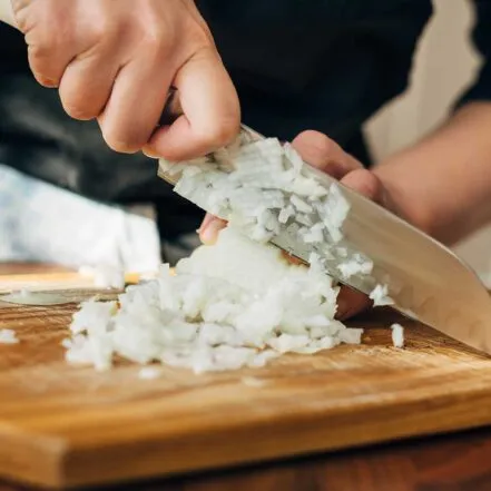 A person's hands demonstrating knife skills, slicing vegetables on a cutting board