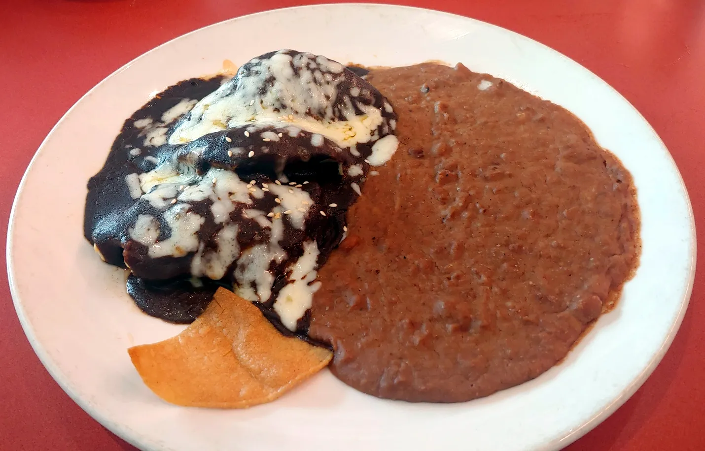 A plate with chicken covered in a dark sauce, rice, and beans