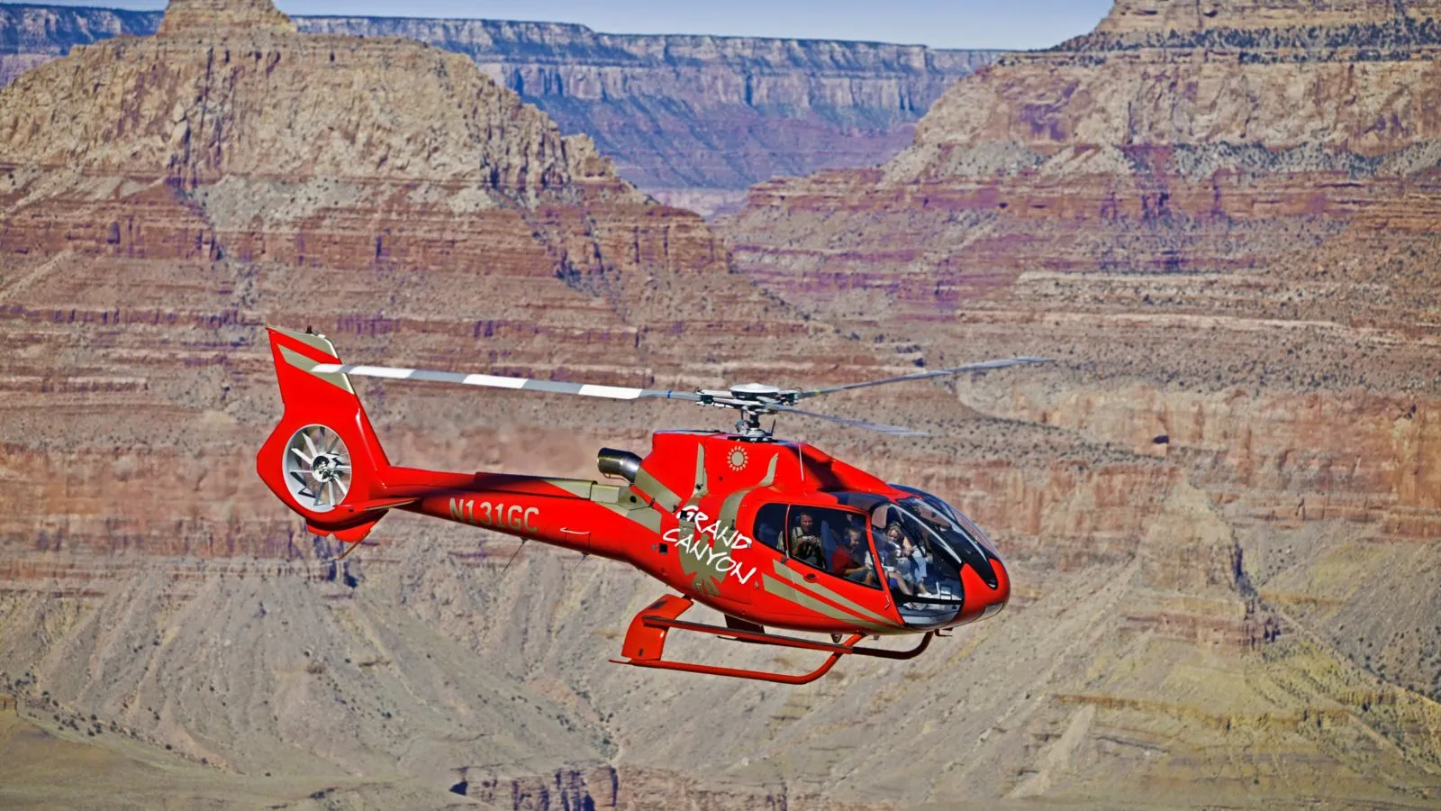 A red helicopter flies over the rugged terrain of the Grand Canyon, offering incredible aerial views.