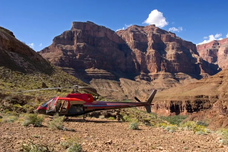 A red helicopter on the ground surrounded by red rock mountains, suggesting adventurous date ideas like helicopter tours near Las Vegas