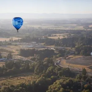 A scenic hot air balloon drifts peacefully above a wooded valley, offering aerial tours near Portland Oregon.
