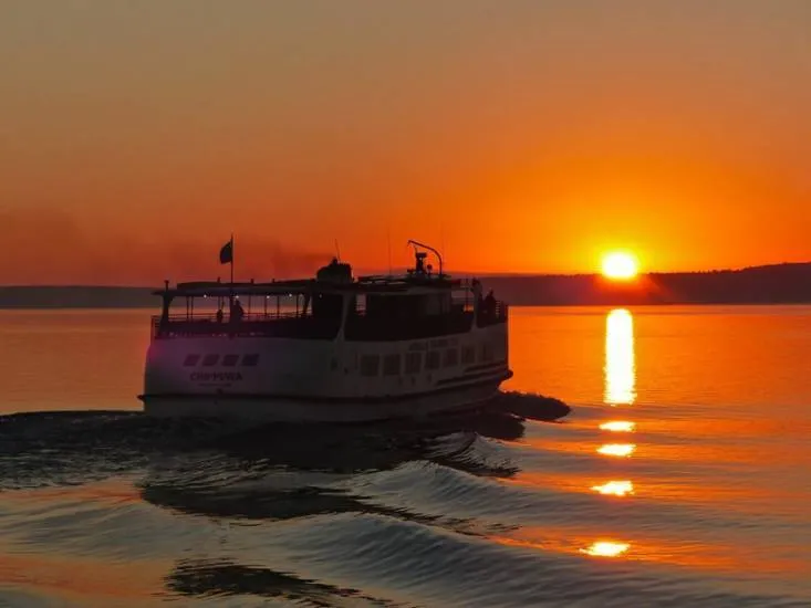A scenic view of a Sip and Sail cruise boat on the water near Mackinac Island at sunset, a relaxing way to explore the beauty of the Great Lakes.