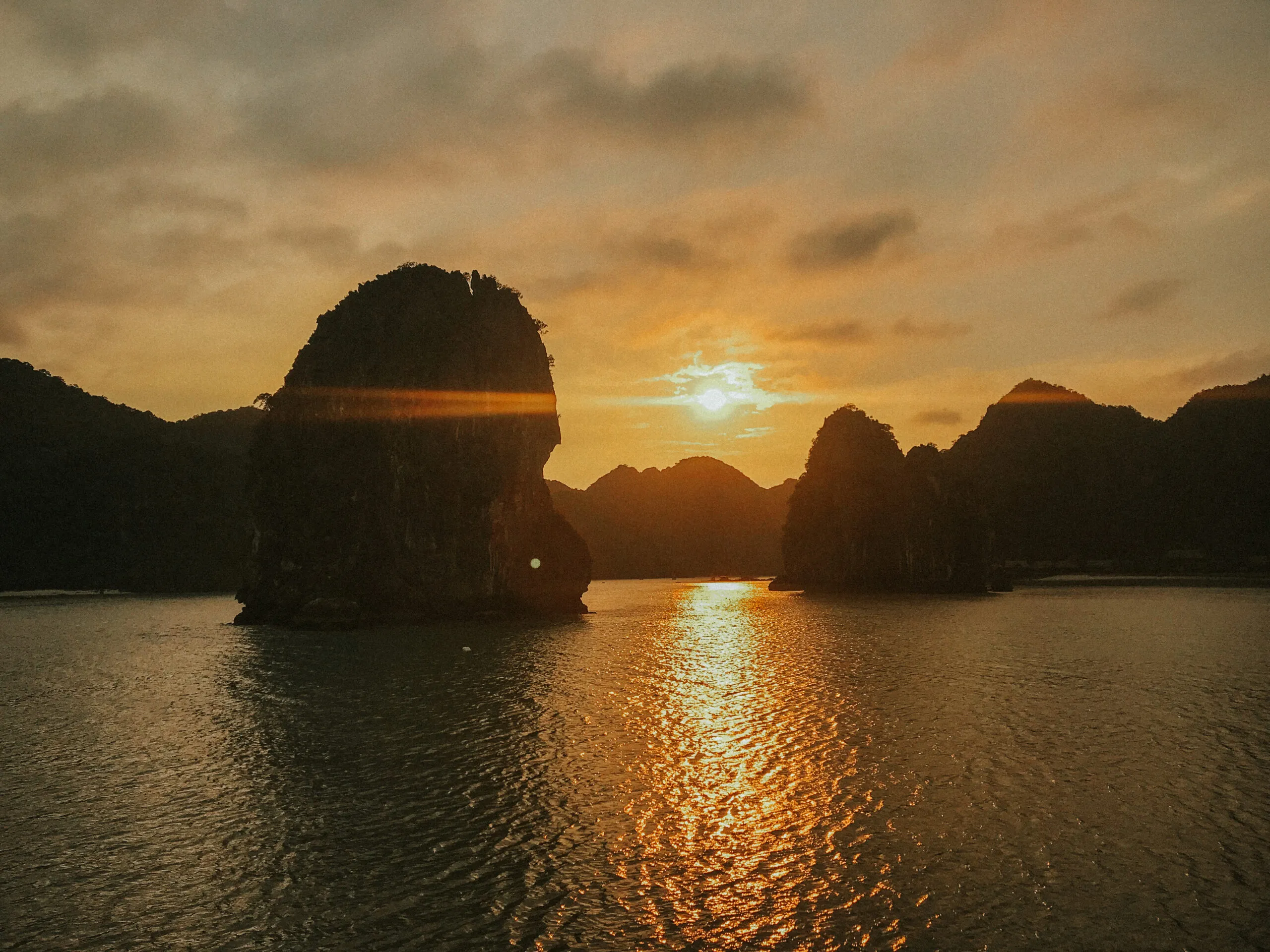 A scenic view of the sunset over the calm waters of Ha Long Bay, with silhouetted karsts in the distance