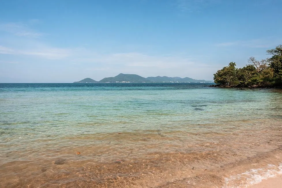 A secluded beach with clear blue water and mountains in the distance