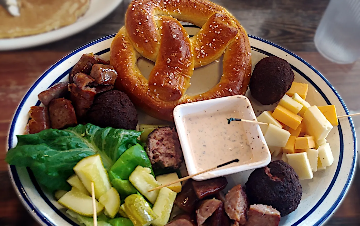 A selection of appetizers on a plate, including a pretzel, sausage, and round fritters