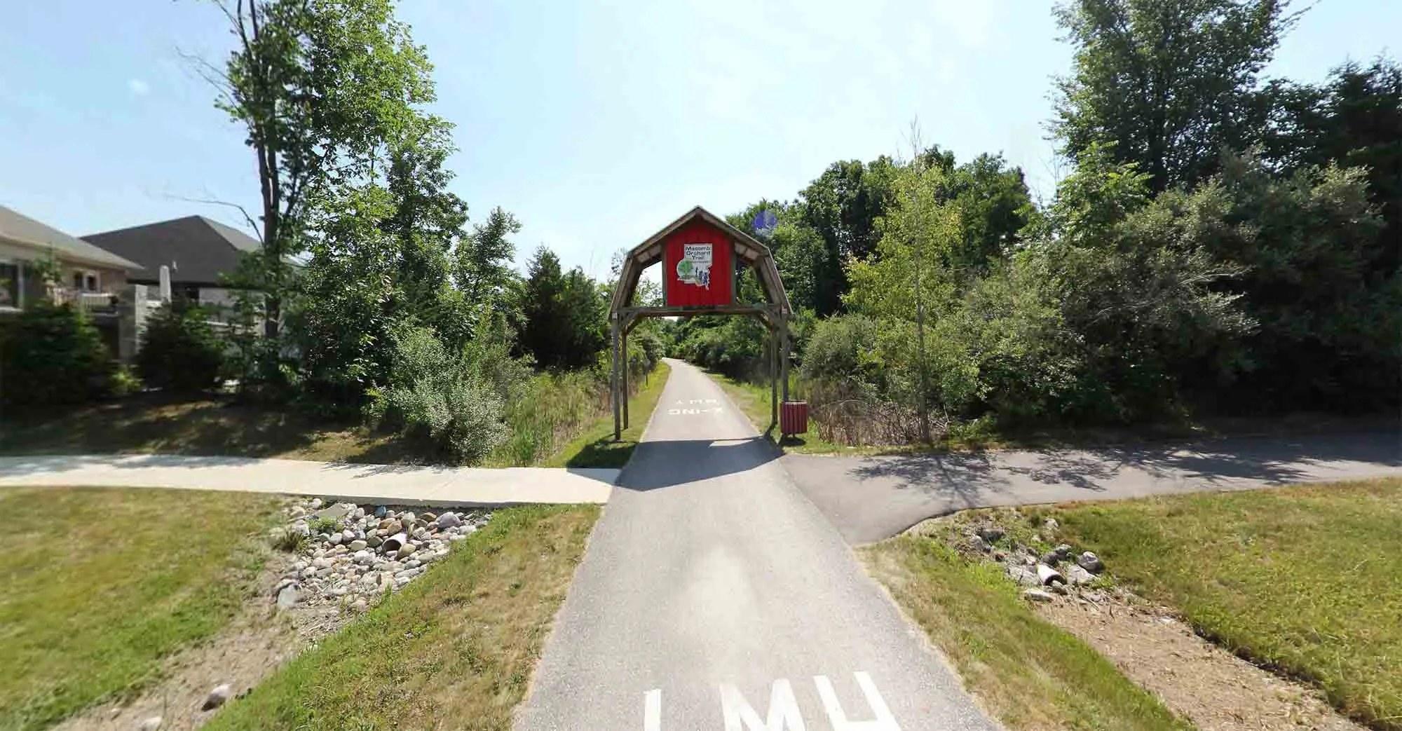 A straight, paved trail bordered by trees and open fields, characteristic of the Macomb Orchard Trail