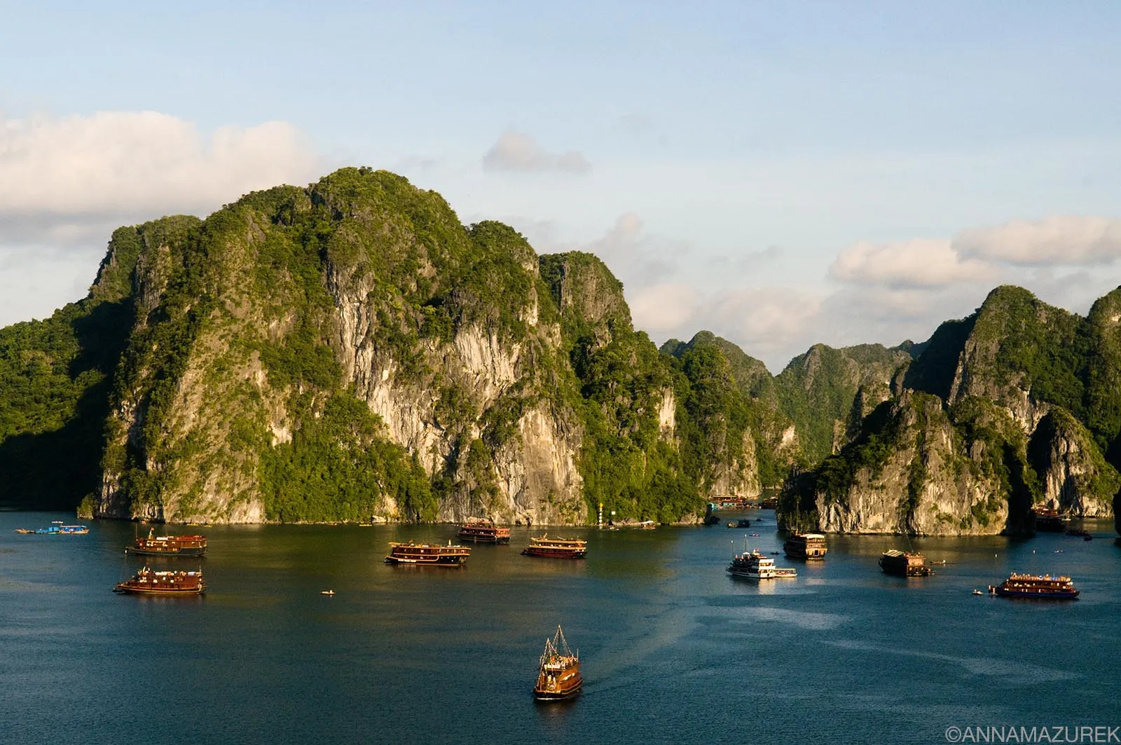 A stunning panoramic view of limestone karsts rising from the emerald waters of Ha Long Bay, Vietnam, under a blue sky.