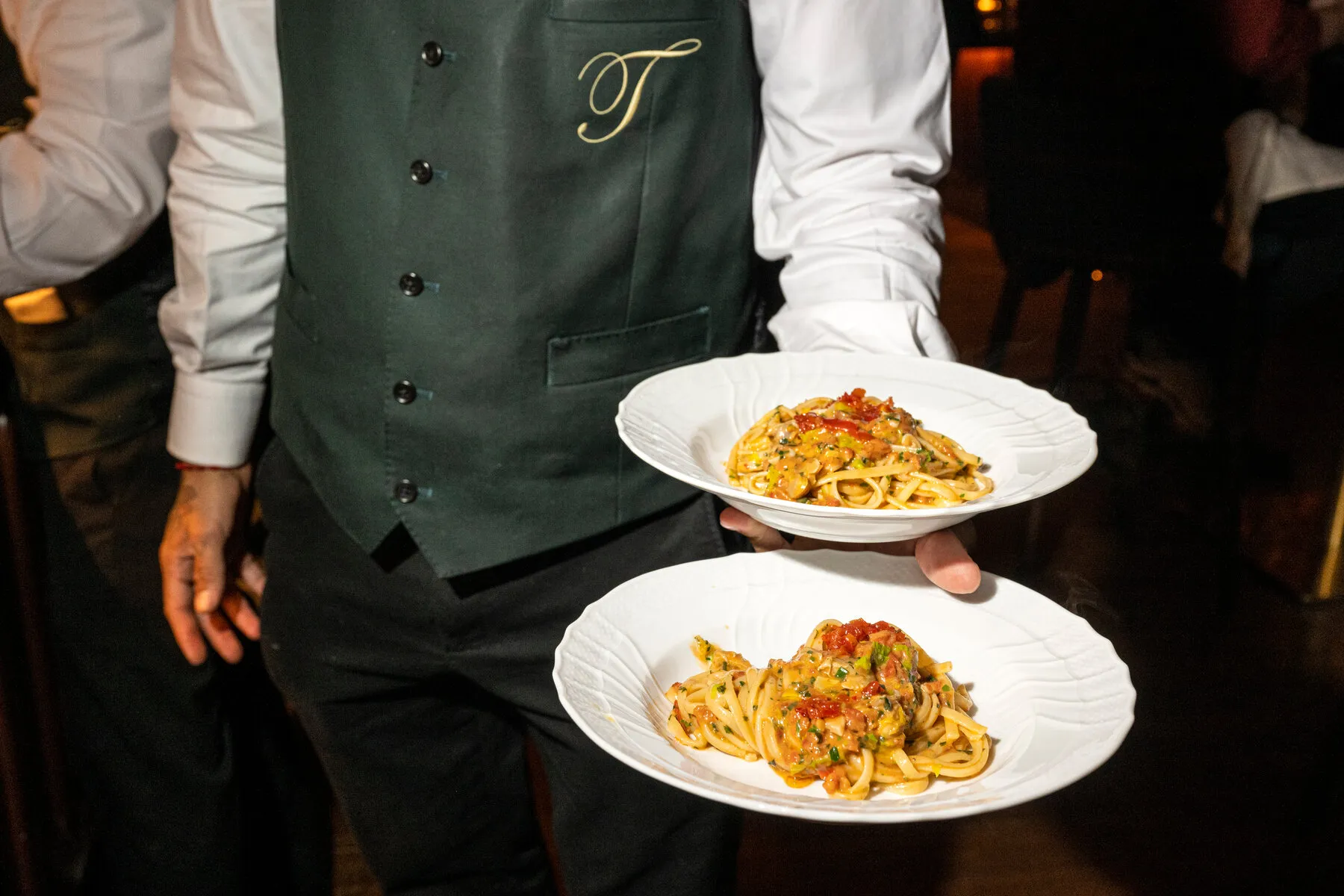 A waiter at Torrisi carrying two plates of linguine, illustrating the service and presentation style of this Italian restaurant.
