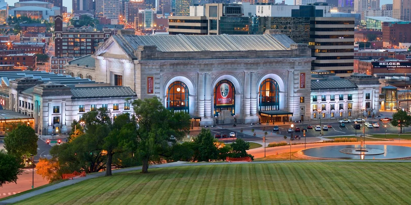 Alt text: An outdoor plaza in Kansas City, Missouri, featuring an ornate fountain with sculptures spraying water, surrounded by trees and buildings.