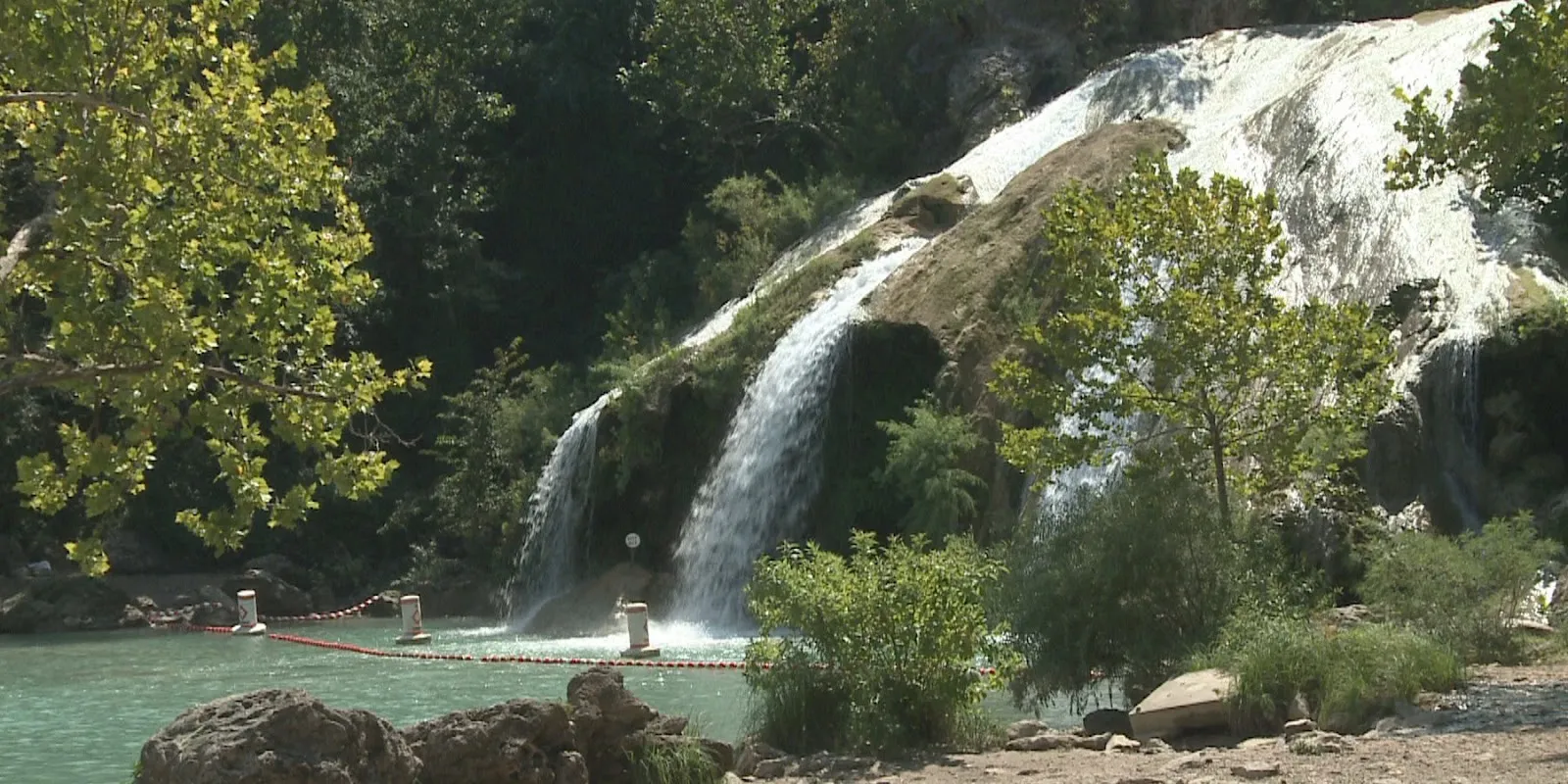 Alt text: Turner Falls waterfall in Oklahoma cascading down a rocky cliff face into a pool below, surrounded by trees.