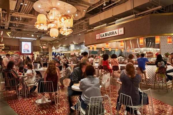 An aerial view of Mercado Little Spain, showcasing the layout of the food hall with various kiosks and seating areas.