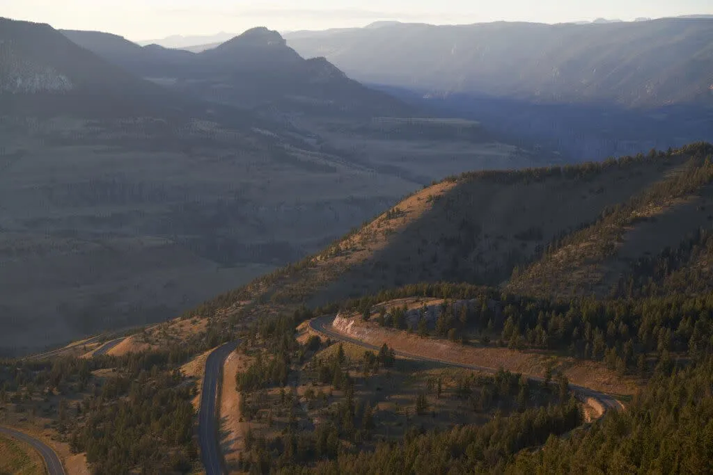 An overhead view of a scenic byway winding through a a hilly landscape covered with trees.