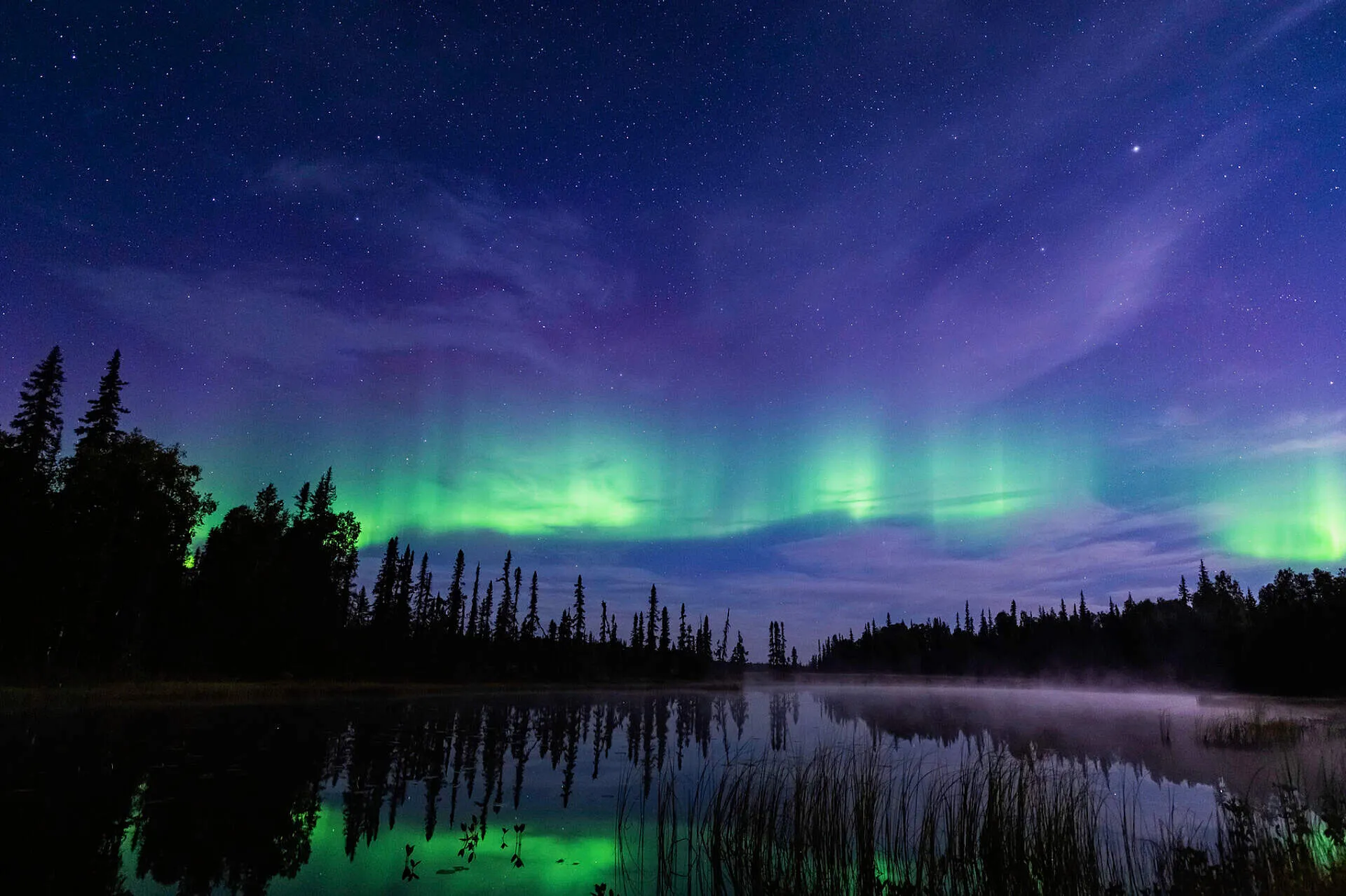 Aurora borealis over a lake in Alaska with mountains in the background.