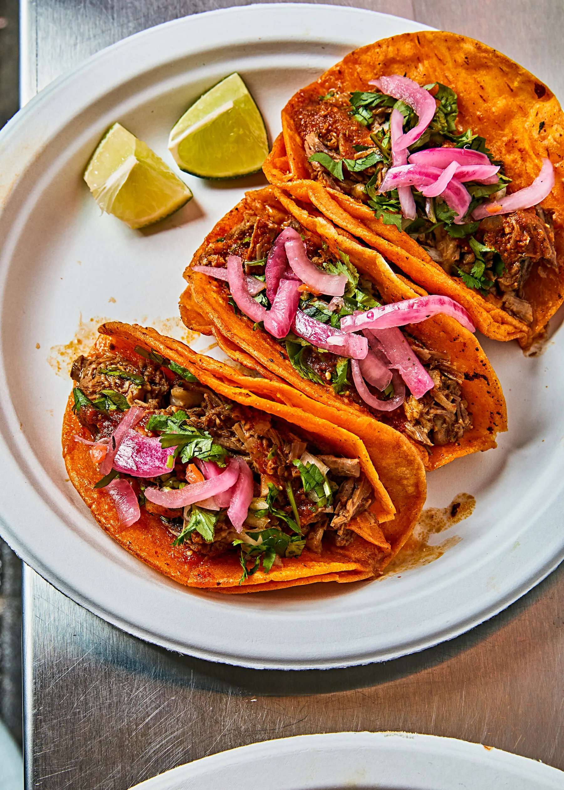 Birria tacos and consomé from Birria-Landia served on a tray, showing the dipping sauce and toppings.