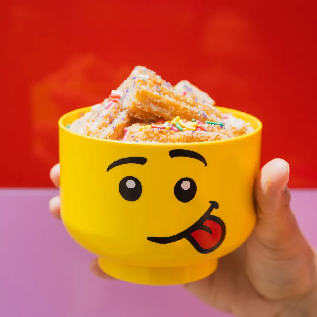 Bite-sized churros with colorful sugar and sprinkles in a themed container.