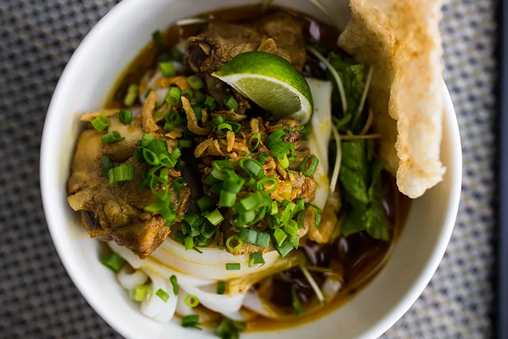 Bowl of Mì Quảng noodles with toppings and herbs, a specialty of Central Vietnam