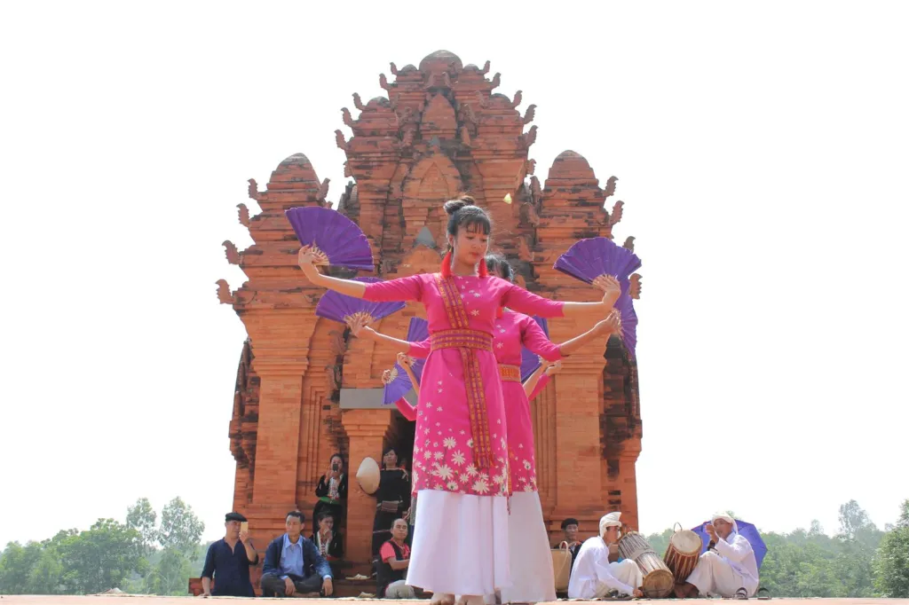 Cham people performing a traditional dance in front of a replica Cham tower