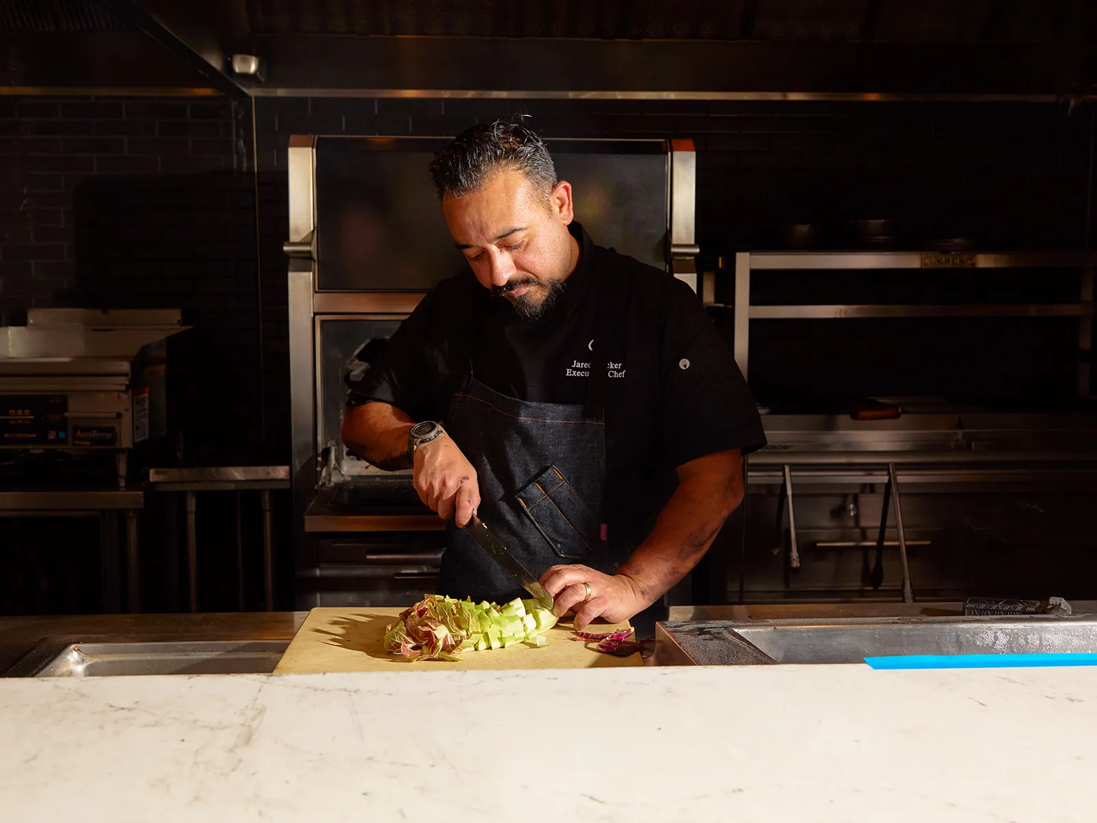 Chef in black chef coat with apron chopping cabbage in restaurant kitchen