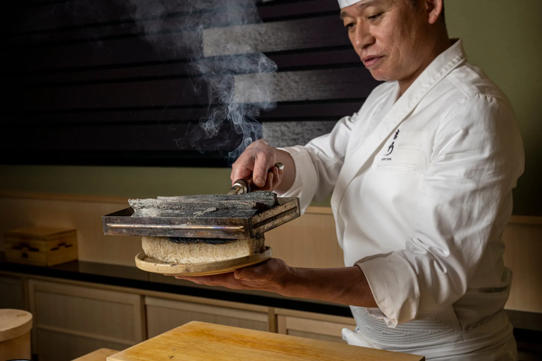 Chef Tadashi Yoshida searing mackerel sushi with hot charcoal at Yoshino, a signature moment in his precise Japanese omakase.