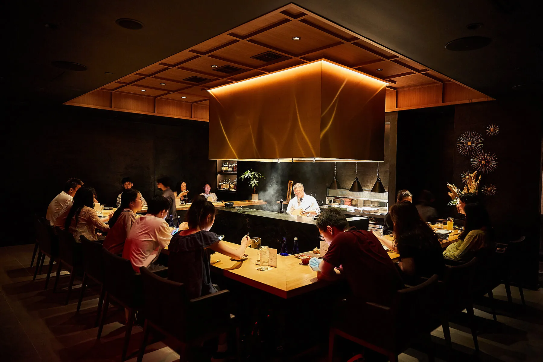Diners seated around the counter watching Chef Atsushi Kono prepare yakitori at Kono, emphasizing the close interaction.