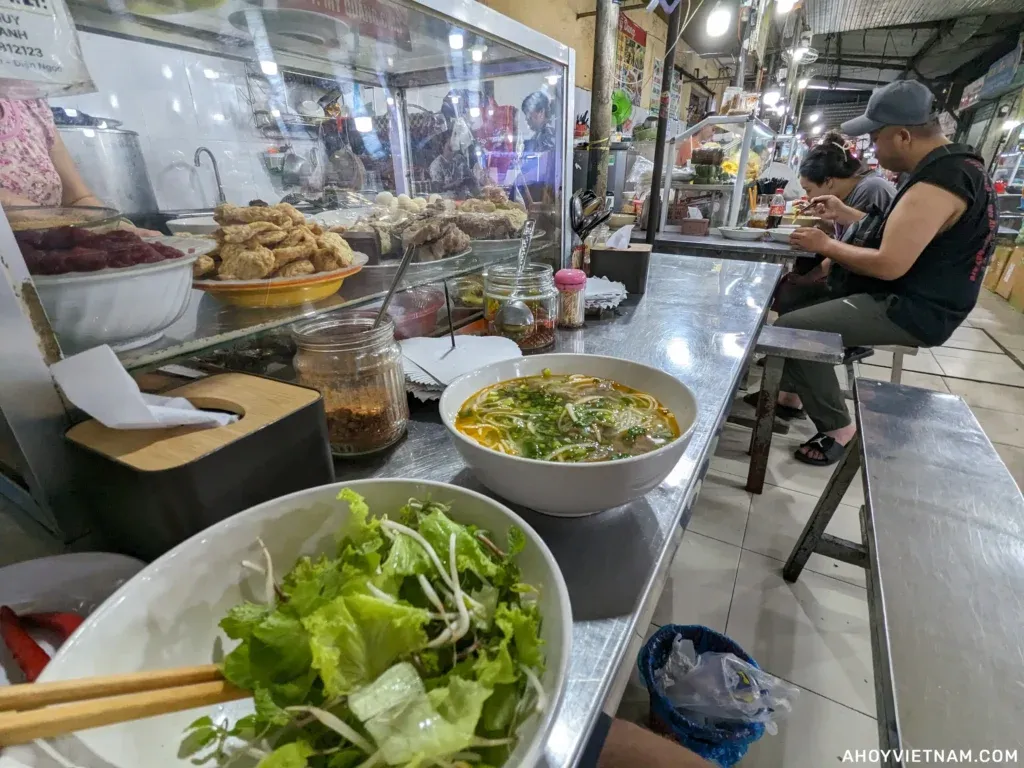 Eating bun bo Hue at a metal table inside My An Market in Da Nang.