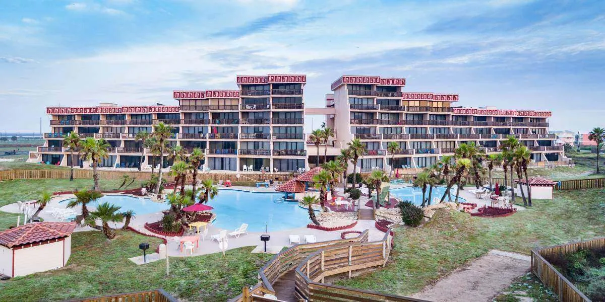 Exterior view of a condo building with pools and beach in the background