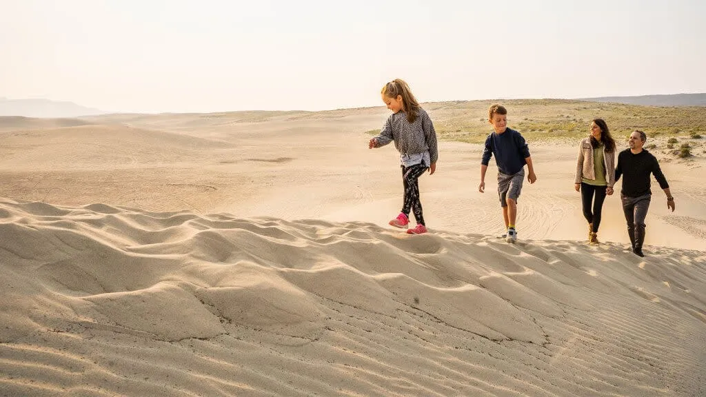 Family climbing a sand dune at the Killpecker Sand Dunes - Adventure Things To See And Do In Wyoming