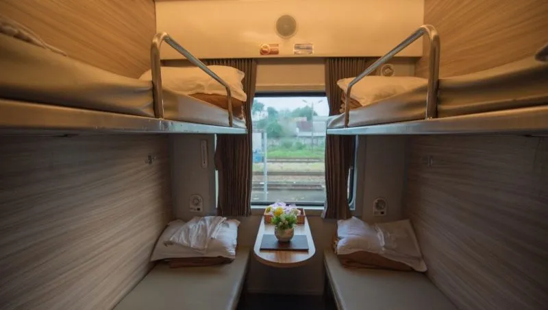 Four bunks adorned with pillows and blankets flank the walls of a small train compartment.