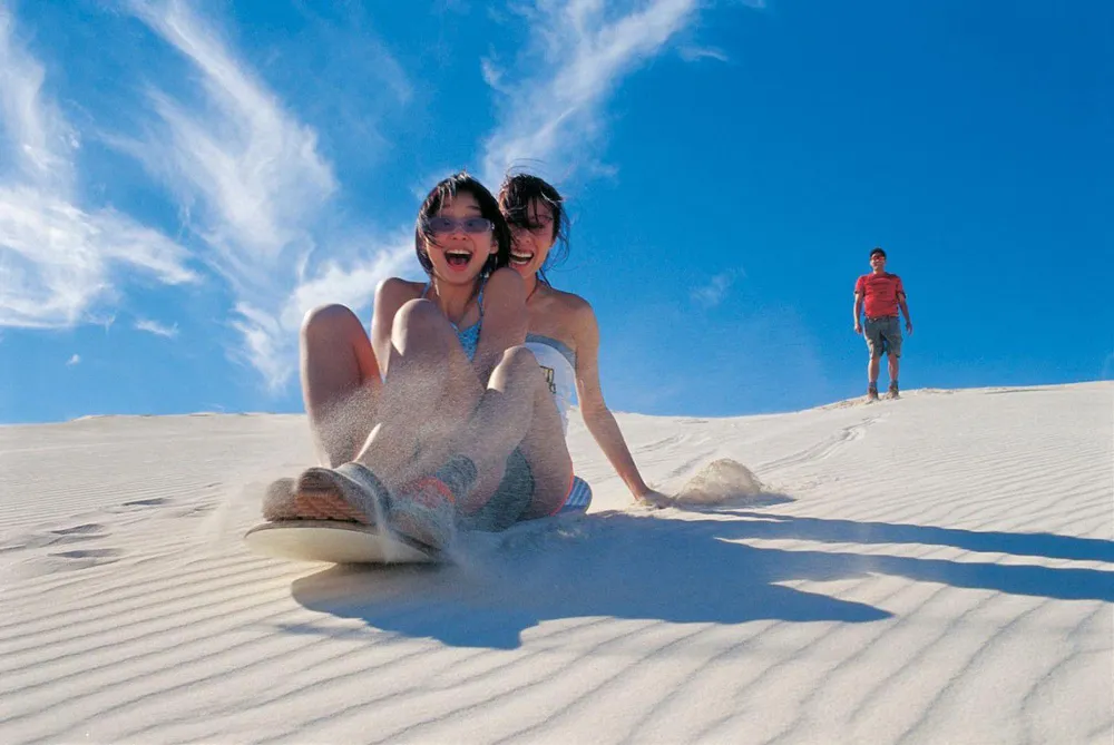 Friends sandboarding down the red dunes in Mui Ne, a fun outdoor activity in Vietnam